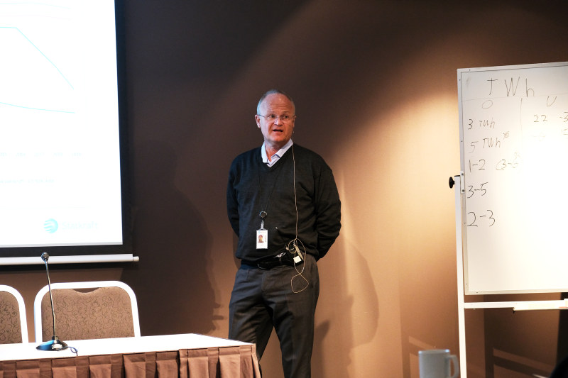 Mann med hendene bak ryggen, snakker til forsamling. foto