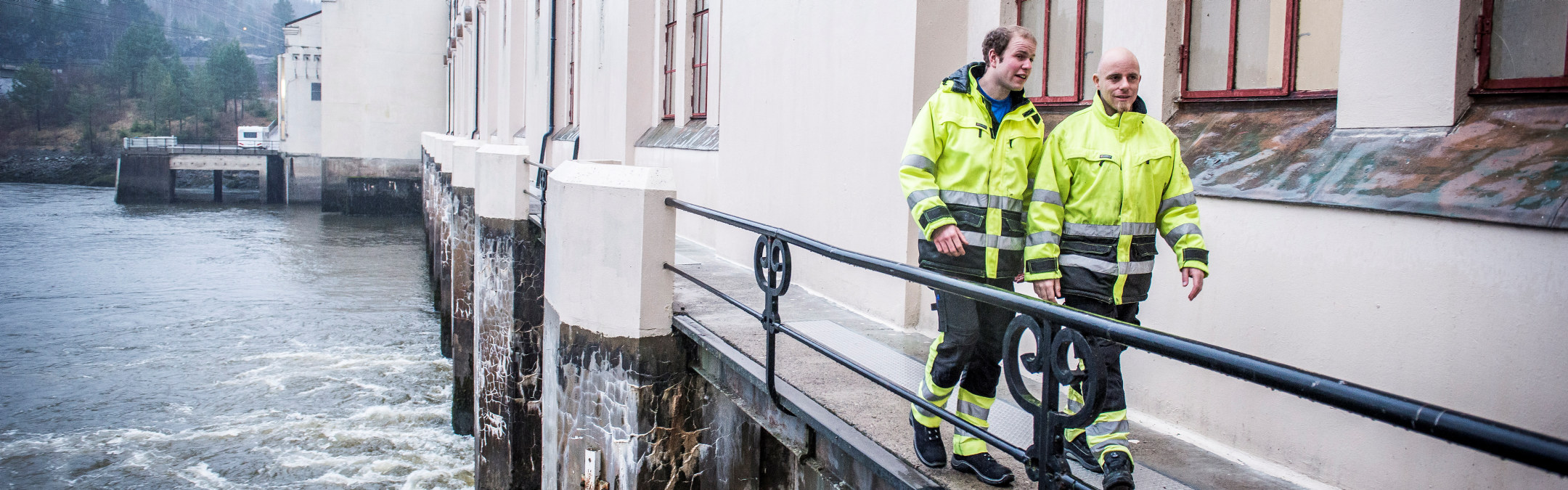 Foto: To menn i arbeidsdress går langs Vamma kraftstasjon.