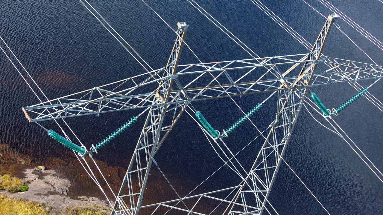 Foto: Kraftmast med linjer som strekker seg over et vann. 