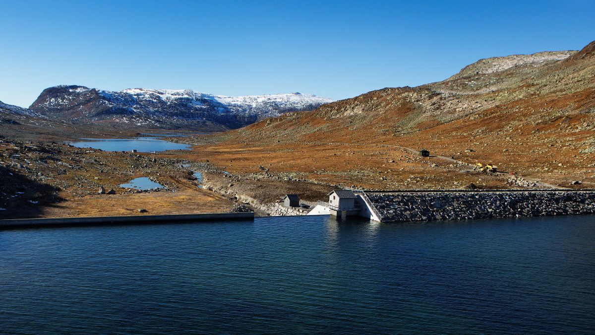 En dam, et lite hus og fjell. Foto