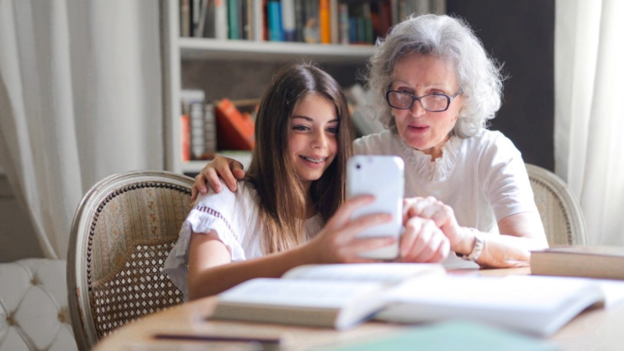 Foto: En jente og en eldre dame sitter sammen og ser på en mobilskjerm. Foto: Andrea Piacquadio /Pexels 

