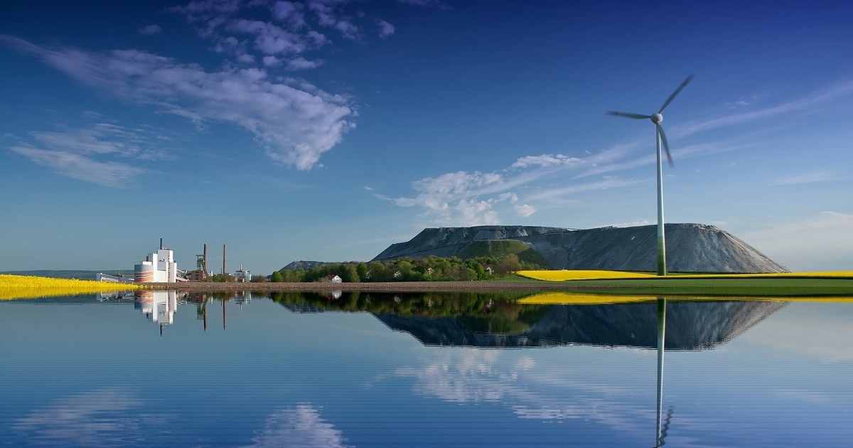 En innsjø ved foten av et fjell, industri, en vindmølle og en åker