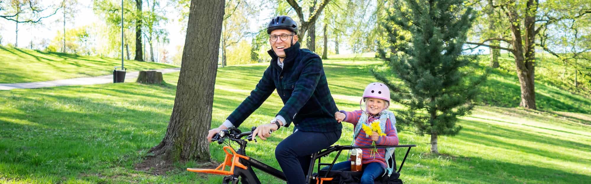  En mann sykler på en elsykkel med en jentunge som sitter bakpå