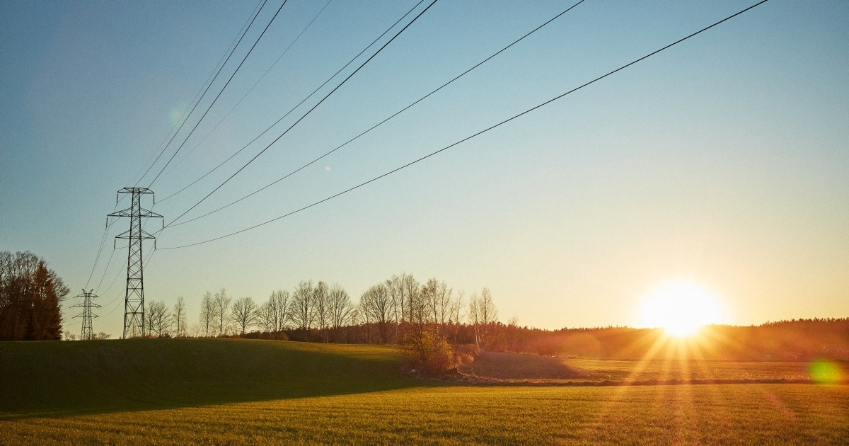 Strømmast over et jorde i solnedgang