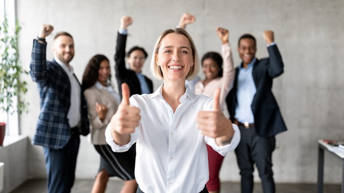 Businesswoman Gesturing Thumbs-Up Standing With Joyful Employees Team In Office