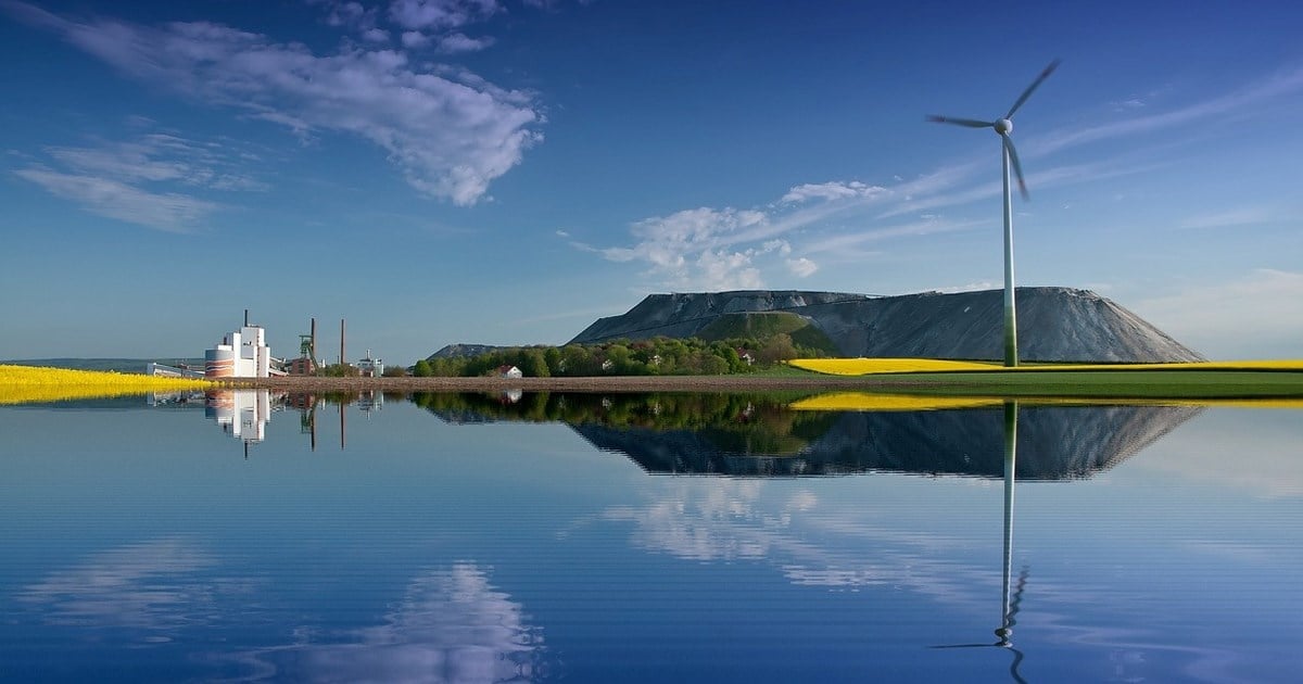 En innsjø ved foten av et fjell, industri, en vindmølle og en åker
