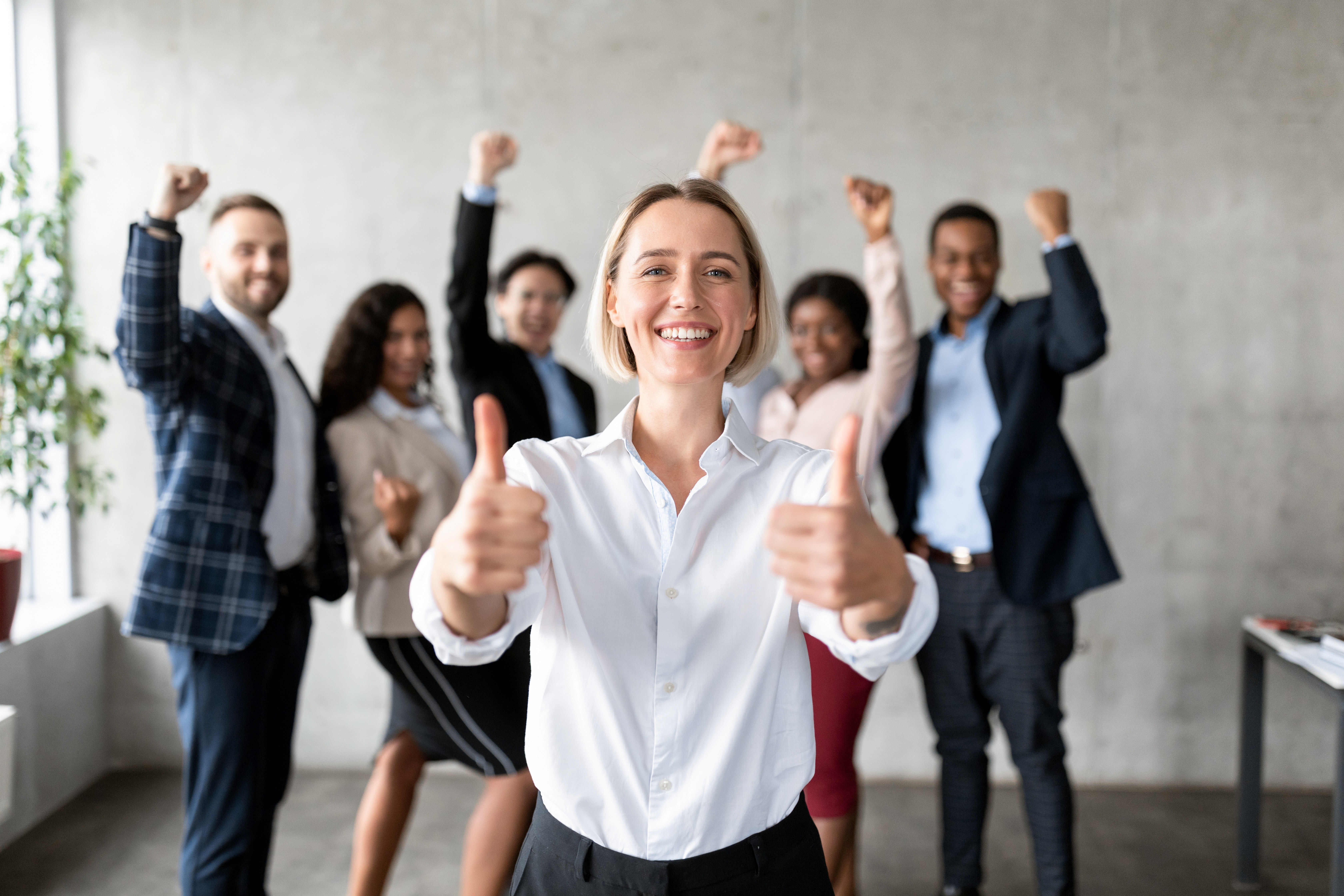 Businesswoman Gesturing Thumbs-Up Standing With Joyful Employees Team In Office