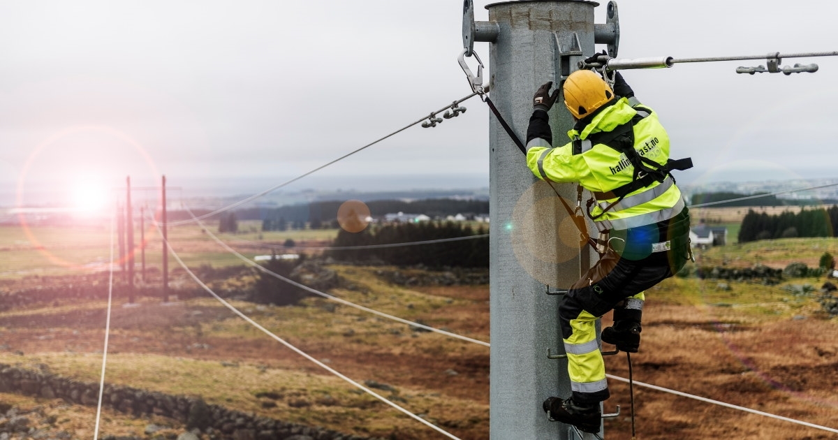 En energimontør jobber oppe i en kraftmast på et jorde. Foto