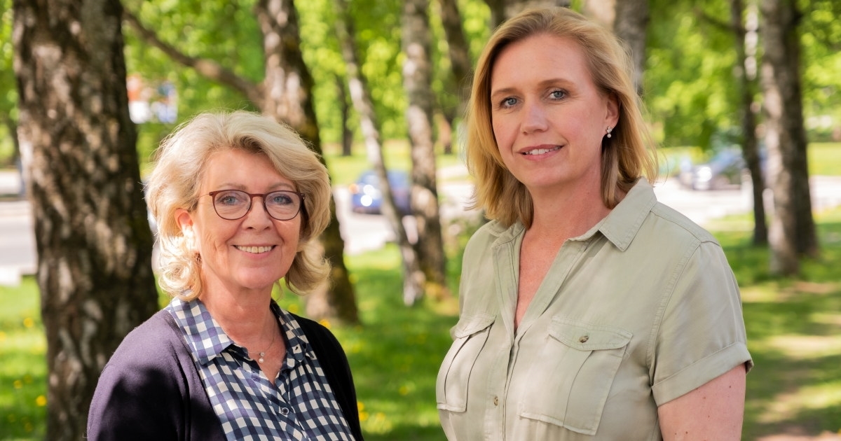Bilde av Åslaug Haga og Trine Kopstad Berentsen utendørs med grønne bjørker i bakgrunnen og i finevær.