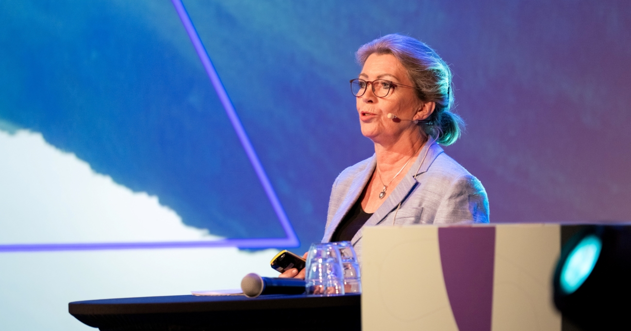 Bilde av Åslaug Haga som snakker fra scenen under årskonferansen 2025.