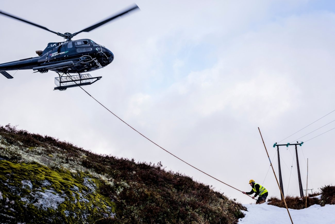 Helikopter og en mann som jobber med en kraftmast. Foto