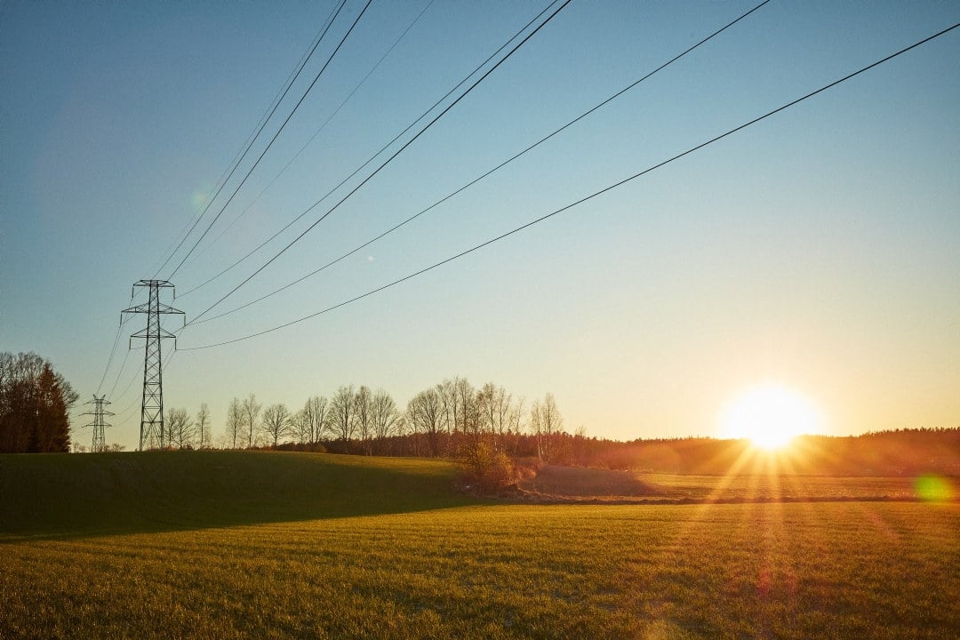 Strømmast over et jorde i solnedgang