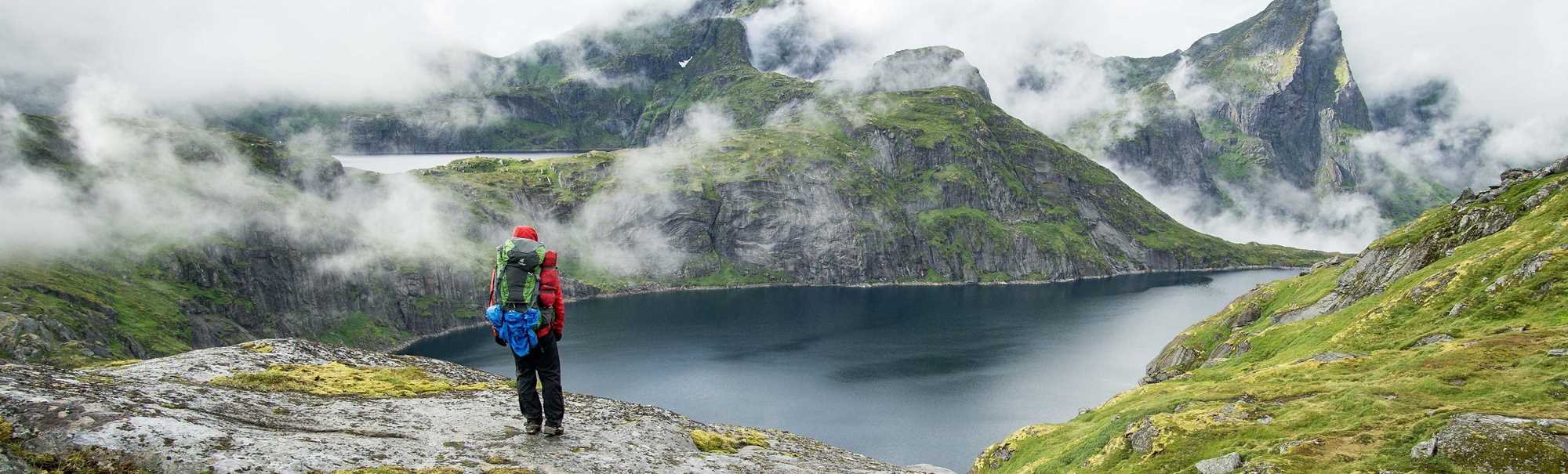 Person med stor ryggsekk ser utover fjell og vann. Foto