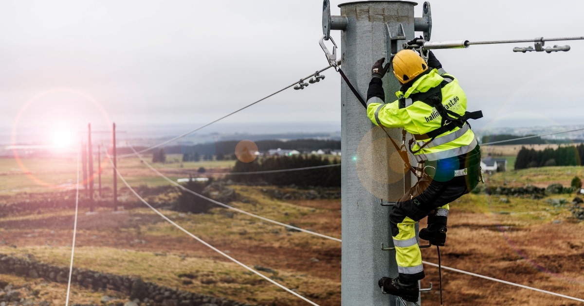 En energimontør jobber oppe i en kraftmast på et jorde. Foto