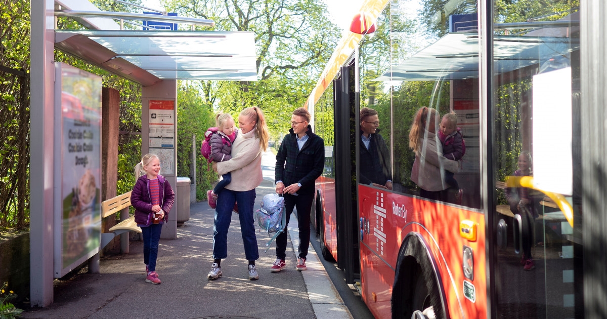 To små jenter, en mor og en far skal gå inn på en buss.